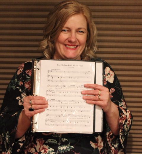 Author holding a binder holding sheet music of song she wrote